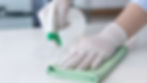 Gloved hands wiping a surface with a rag and spray bottle.