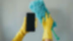Hands with latex cleaning gloves holding up a microfiber duster and a smartphone.